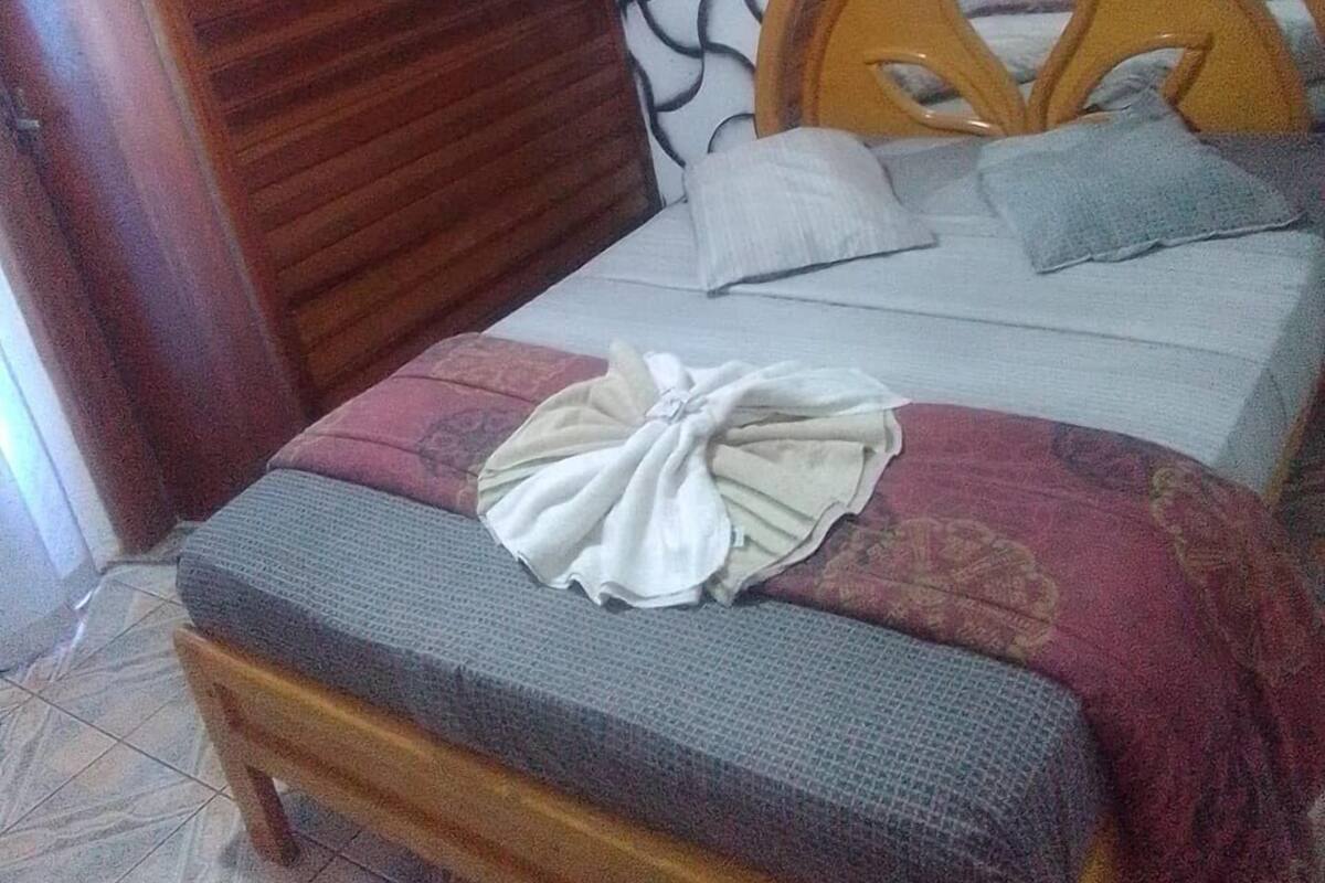 Uma cama com cabeceira de madeira, uma toalha branca bem dobrada e um edredom estampado.