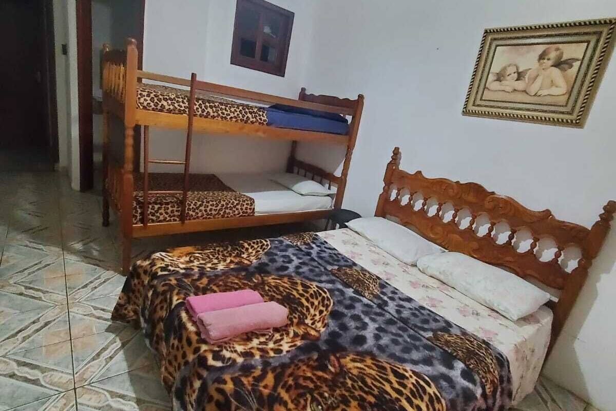 Quarto com uma cama e um edredom estampado com padrão de leopardo, uma cama beliche de madeira, um ventilador de teto e uma moldura com um quadro na parede.