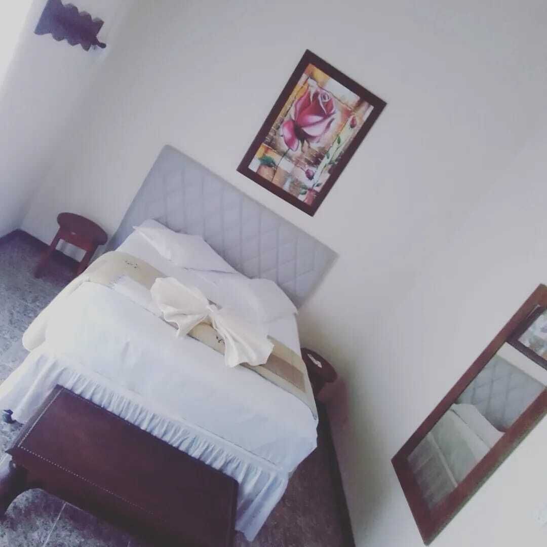 Uma cama bem arrumada com cabeceira, um banquinho de madeira e um quadro na parede.