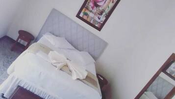 Uma cama bem arrumada com cabeceira, um banquinho de madeira e um quadro na parede.