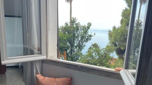 Un racó acollidor amb una banca, vista al mar i una finestra amb cortines.