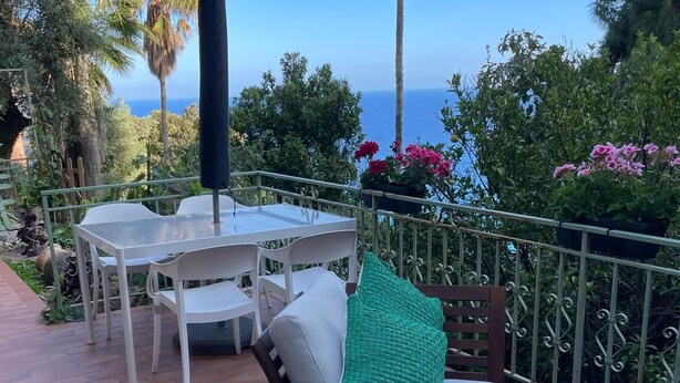 Un pati amb taula i cadires, una banca amb coixins, i vista a l'oceà.