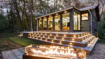 En moderne hytte med glasfacade, træterrasse og bålsted.