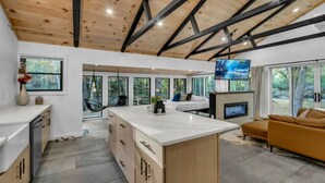 A modern kitchen with a large island, a dining area with a sofa, and a fireplace. - LUX Designer Private Waterfront Crooked River SEBAGO - GLASS WALLS - Huge Yard (Naples)