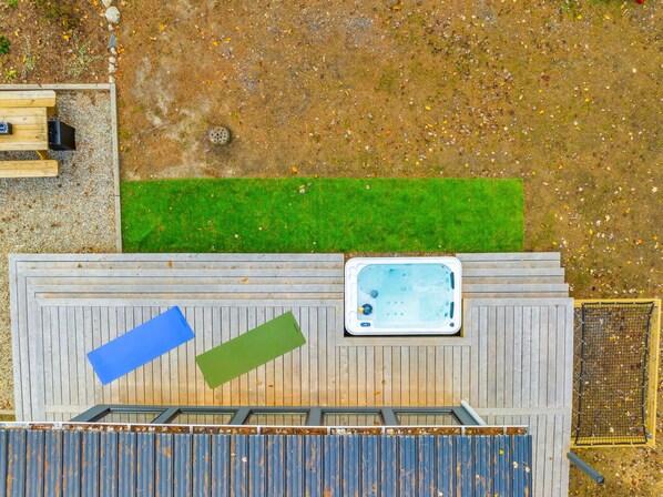 A hot tub on a wooden deck with a small grassy area and a wooden fence in the background.