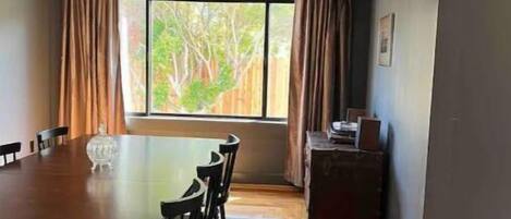 A dining area with a wooden table and chairs, a small cabinet, and a window with curtains.