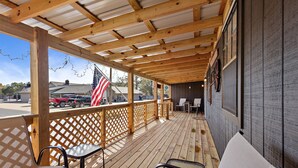A covered outdoor seating area with wooden beams and lattice railings, featuring tables and chairs.