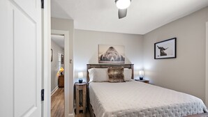 A bedroom with a large bed, two bedside tables with lamps, a ceiling fan, and two framed pictures on the wall.