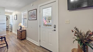 A hallway with a white door, a framed picture, a small table with a lamp, and a potted plant.
