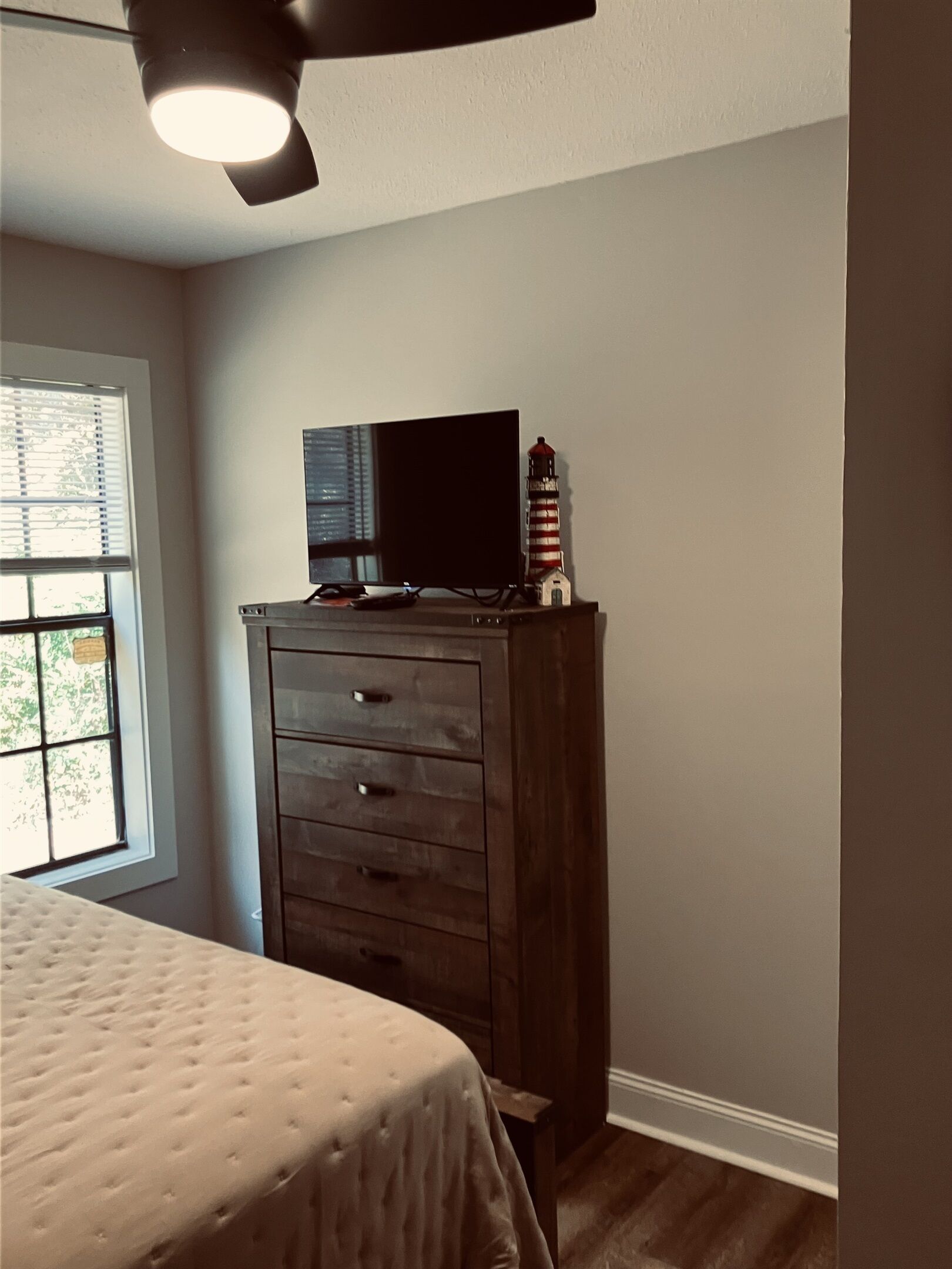 A bedroom with a bed, a dresser, a television on top of the dresser, and a window with blinds.