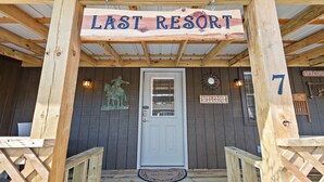 A wooden structure with a sign reading "LAST RESORT" above a door, a welcome mat, and a number "7" on the wall.