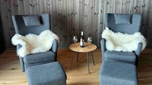 Een kamer met twee grijze fauteuils, een kleine ronde houten tafel met twee wijnglazen en een fles, en een houten wand met verticale latten.