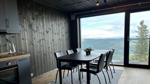 Een moderne eetruimte met een grote tafel en stoelen, een houten vloer en een uitzicht op bergen door een groot raam.