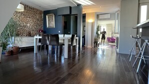 Un vaste espace de vie doté d’un plancher en bois foncé, d’une table à manger avec des chaises, d’un coin cuisine et d’un escalier menant à un niveau supérieur.