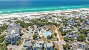Oversigtsbillede af et kystnært boligområde med et stort bygningskompleks, en swimmingpool og en strand.