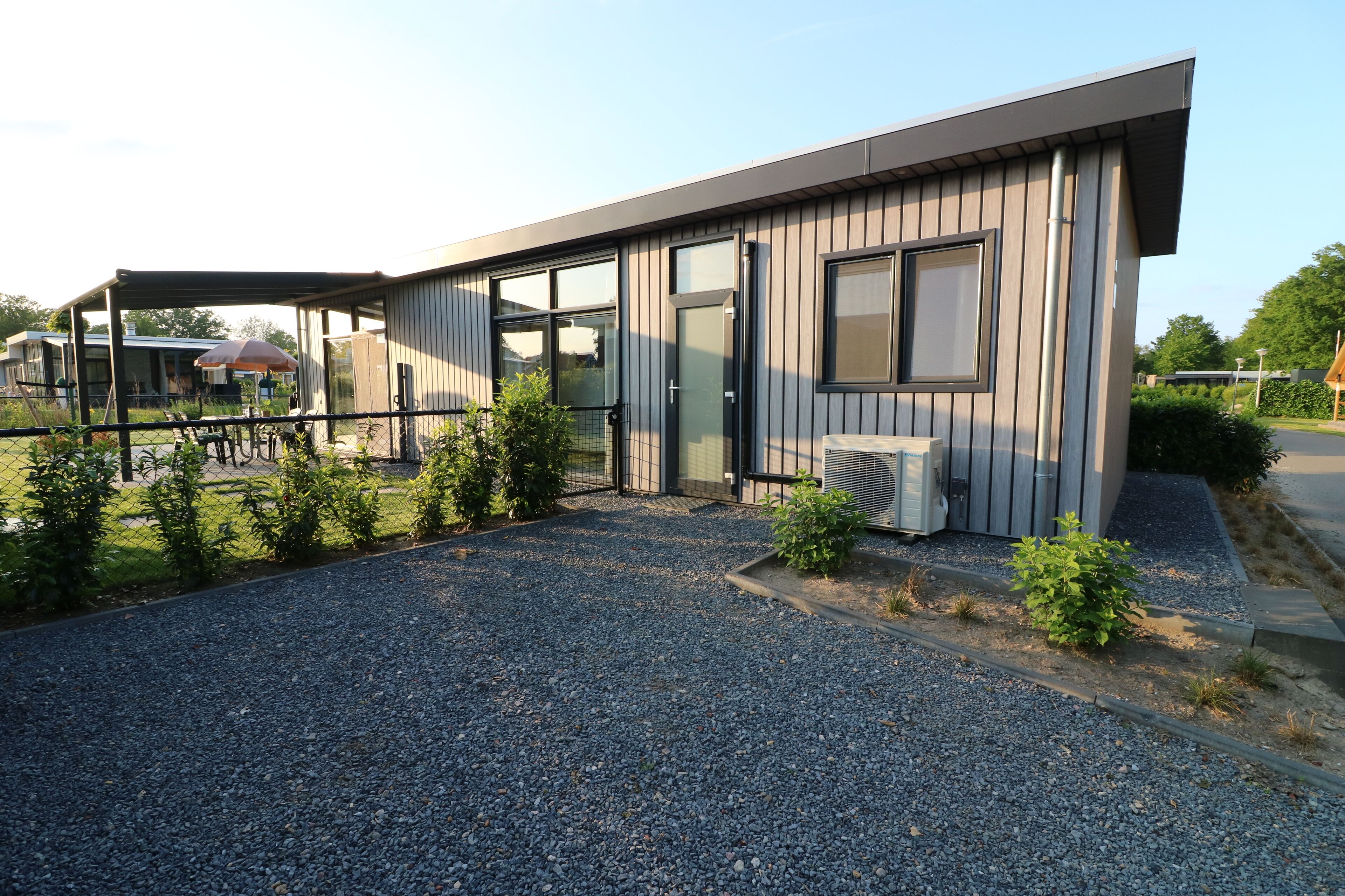 A modern building with large windows, a covered outdoor area, and a gravel driveway.