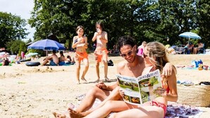 Escena de playa con gente relajándose sobre toallas y leyendo.