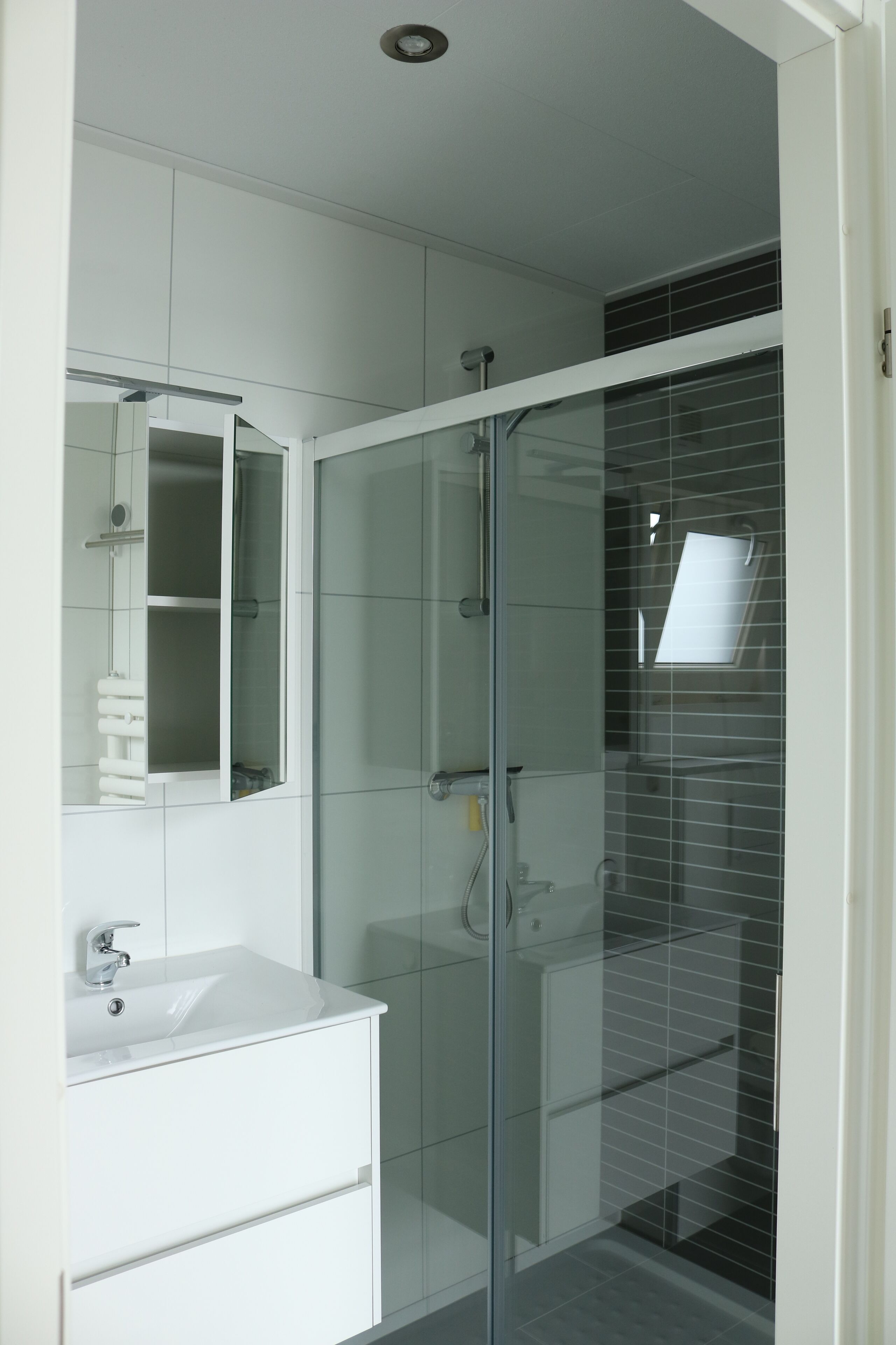 A modern bathroom with a glass shower enclosure, a white vanity with a mirror, and a tiled floor.