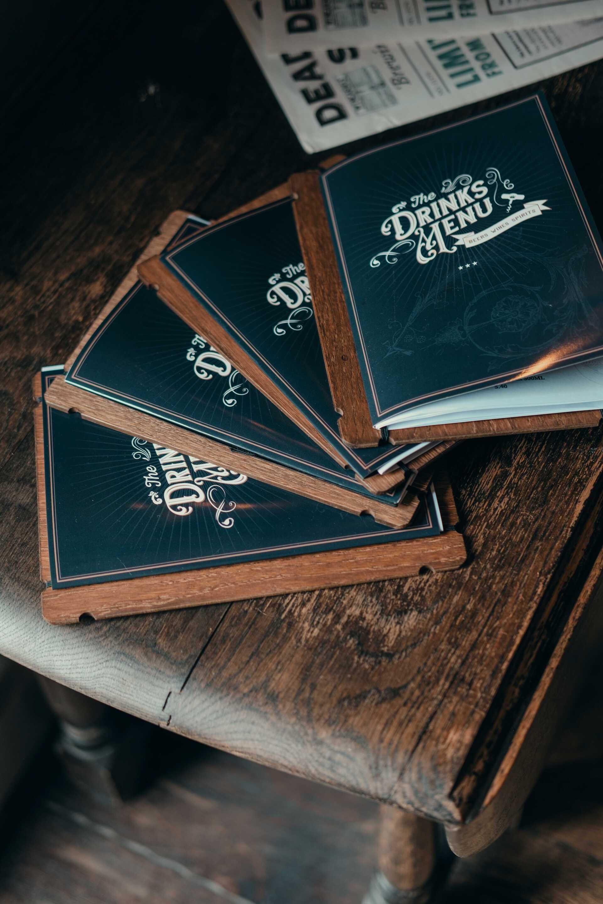 A stack of menu books titled 'The Drinks Menu' on a wooden table.