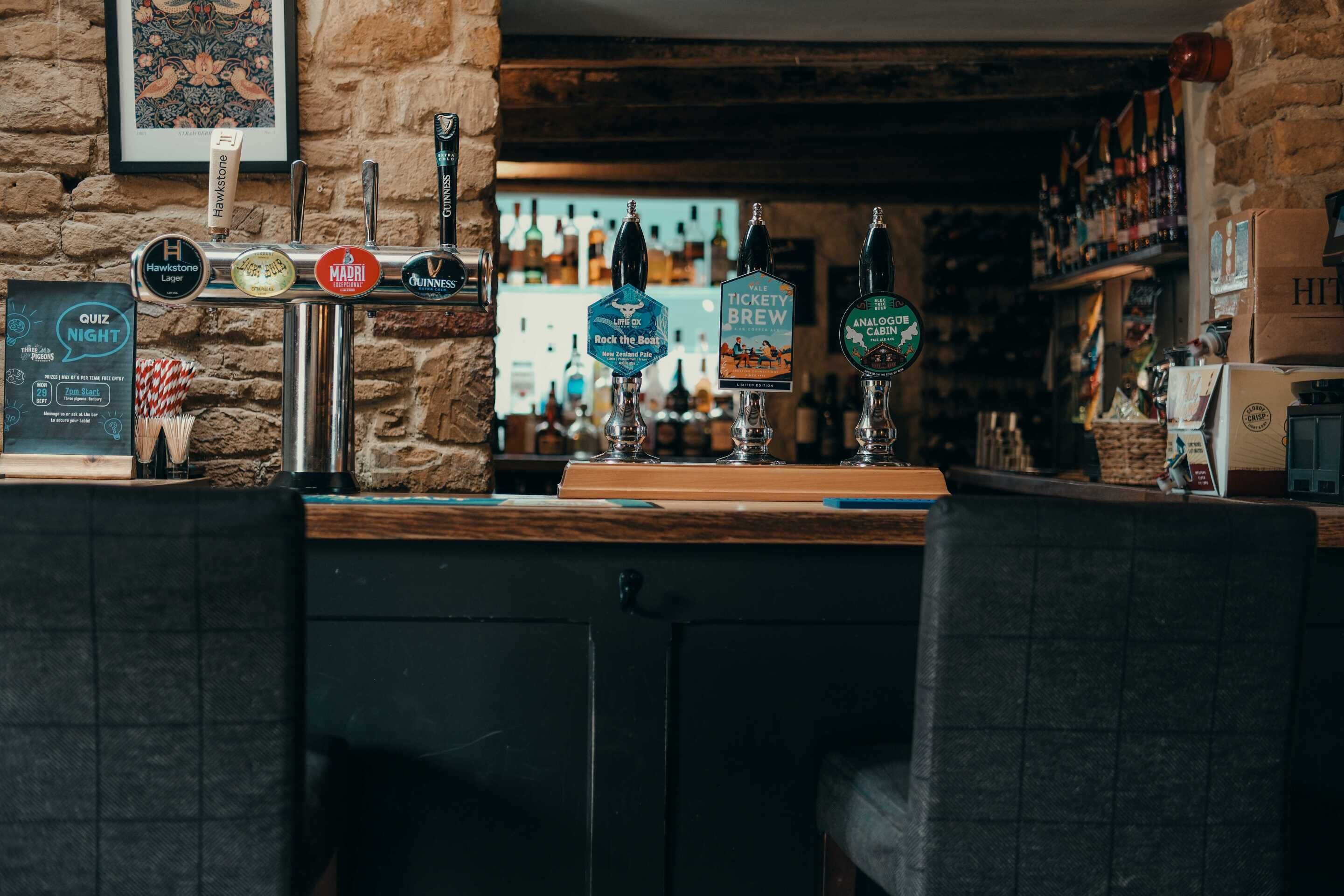 Zona de bar con mostrador de madera, múltiples grifos de cerveza y una variedad de botellas al fondo.