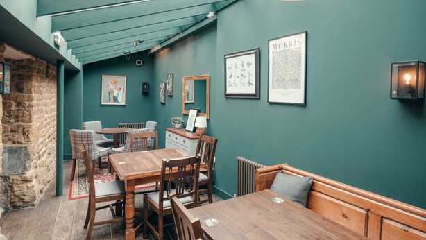 A cozy dining area with a wooden table and chairs, a bench, and a stone wall.