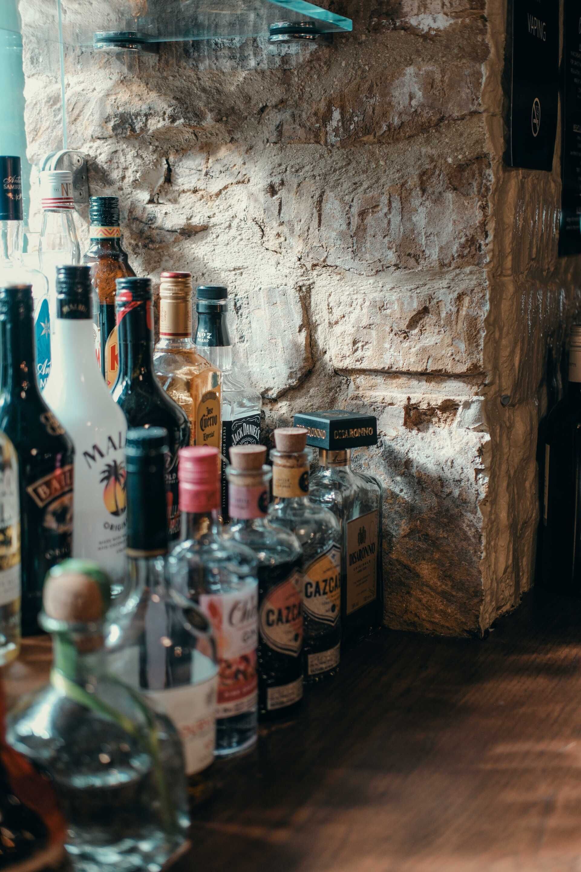Variedad de botellas de licor sobre una barra frente a una pared de ladrillo rústico.