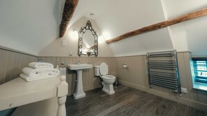 A bathroom with a wooden ceiling beam, a pedestal sink, a toilet, and a towel rack.