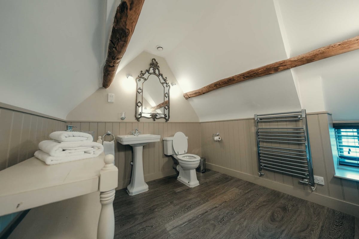 A bathroom with a wooden ceiling beam, a pedestal sink, a toilet, and a towel rack.