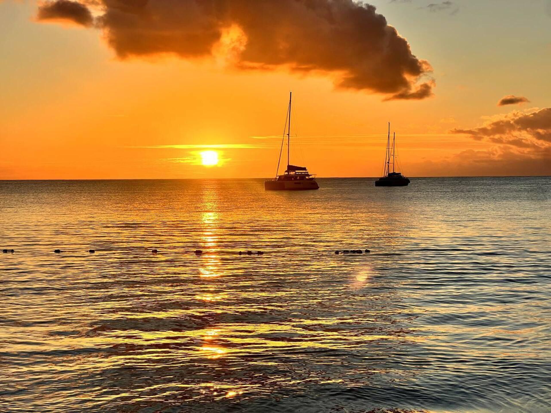 Un coucher de soleil sur une mer calme, avec deux voiliers ancrés.