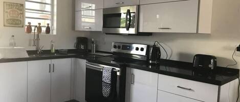 A modern kitchen with white cabinets, a stainless steel stove, a microwave, and a coffee maker.