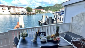 A balcony with a table set for two, overlooking a marina with boats and buildings. - 4 Guests - Stunning View - Pool - South Finger (Jolly Harbour)