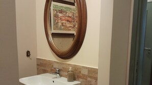 A bathroom with a white sink, a wooden-framed mirror, and a tiled backsplash. - Casa Castelli Holiday Apartment (Bagheria)