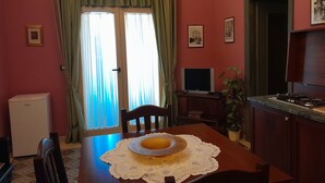 A room with a dining table, chairs, a television, a refrigerator, and a window with curtains. - Casa Castelli Holiday Apartment (Bagheria)