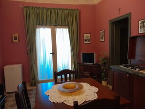 A room with a dining table, chairs, a television, a refrigerator, and a window with curtains. - Casa Castelli Holiday Apartment (Bagheria)
