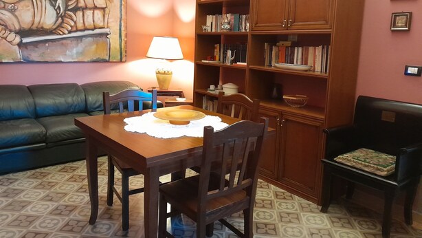 A living room with a dining table, chairs, a sofa, a bookshelf, and a painting on the wall. - Casa Castelli Holiday Apartment (Bagheria)