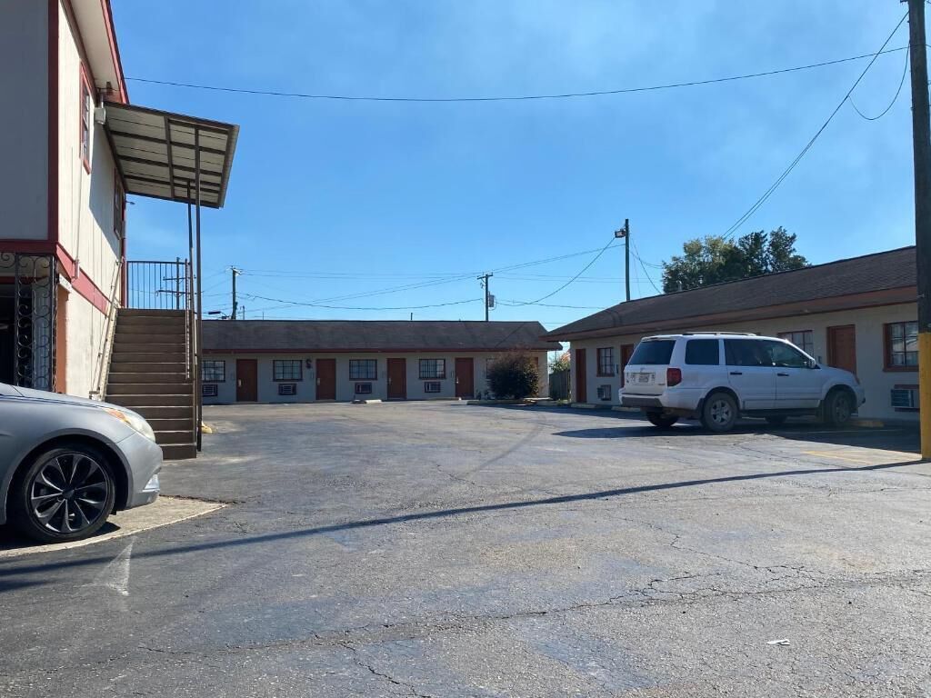 A parking lot with a white van and a car parked in front of a building with multiple doors and a covered entrance.