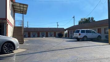 A parking lot with a white van and a car parked in front of a building with multiple doors and a covered entrance.
