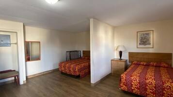 A hotel room with two beds, a wooden floor, a nightstand with a lamp, and a framed picture on the wall.