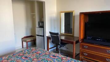 Quarto de hotel com cama, escrivaninha, cadeira, televisão e guarda-roupa.