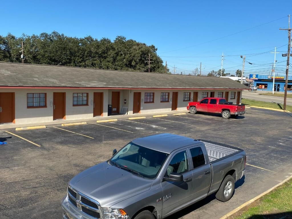 Um motel com estrutura em um único andar, estacionamento e uma caminhonete vermelha estacionada na frente.