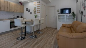 Eine moderne Küche mit Holzausstattung, ein Essbereich mit weißen Stühlen, ein Ledersofa und ein Fernseher auf einem Schrank.