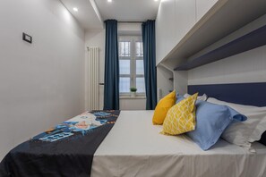 A bedroom with a bed, a window with curtains, a radiator, and a small plant. - Tana del Bianconiglio by Wonderful Italy (Turin)