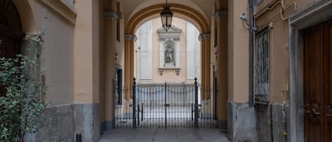 A narrow alleyway with a wrought iron gate, stone pavement, and a statue in the background.