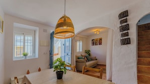 A dining area with a table, chairs, a hanging light fixture, and a view of a living room with a sofa and plants. - Casa del Patito with Vista | Duckling Stays (Olvera)