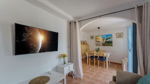 A living room with a flat-screen TV, a white console table, a sofa, a dining area with a table and chairs, and a painting on the wall. - Casa del Patito with Vista | Duckling Stays (Olvera)