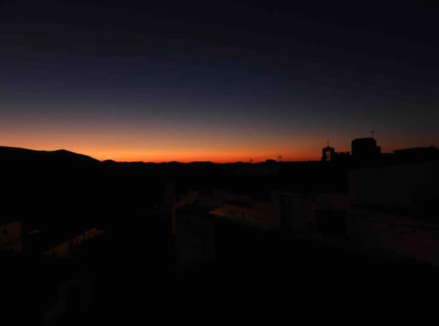 A silhouette of a cityscape at dusk with a prominent church spire.