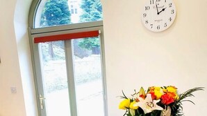 Ein Essbereich mit einem Glastisch, Holzstühlen, einer Uhr, einer Vase mit Blumen, einem Croissant und einem Glas Orangensaft sowie einem Croissant auf einem Teller.