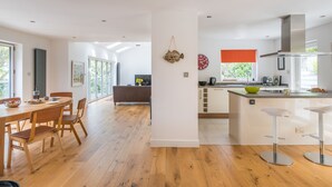 A modern kitchen with a central island, wooden dining table, and chairs. - Stylish 4 bed house walking distance to beaches (Salcombe)