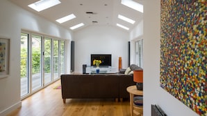 A modern living room with a large TV, a sofa, and a colorful wall art. - Stylish 4 bed house walking distance to beaches (Salcombe)
