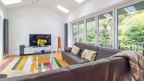 A modern living room with a leather sofa, a flat-screen TV, and a colorful striped rug. - Stylish 4 bed house walking distance to beaches (Salcombe)